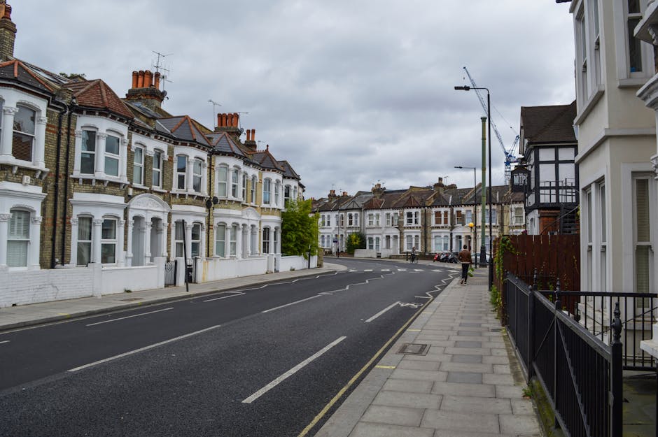 A street scene in Crouch End, Haringey, during daylight hours with a clear blue sky and some scattered clouds. On the left side, a row of historic brick terraced buildings houses various shops, includ