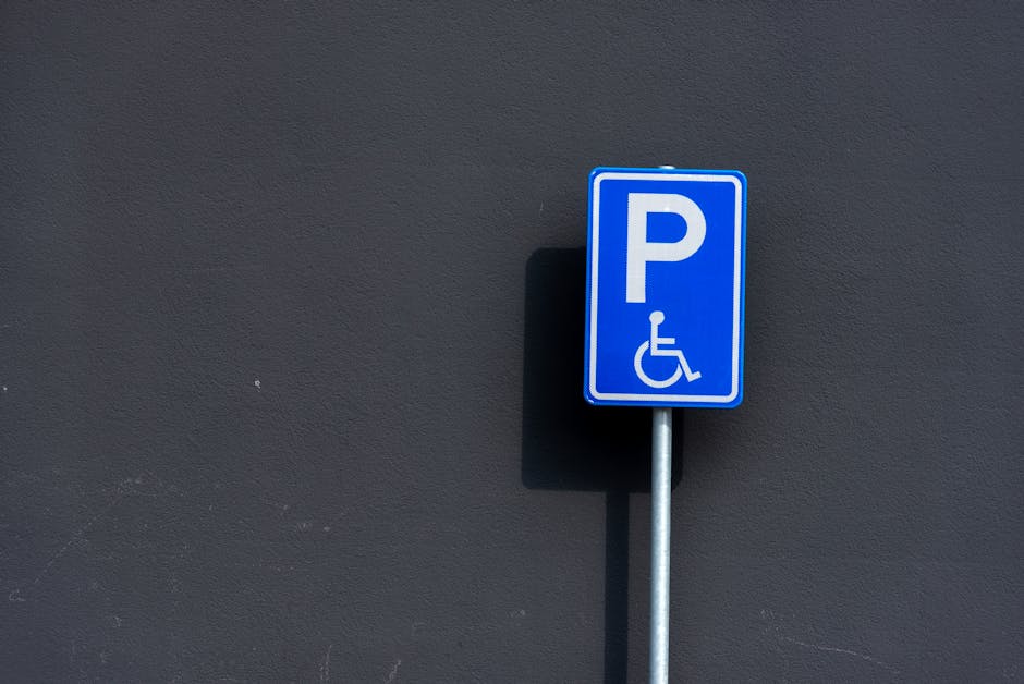 Two red Cheltenham Borough Council parking permit signs indicating an alcohol-free zone are mounted on a black metal pole outdoors, with a blurred background of trees and sunlight. The signs display t